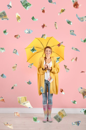 Woman with yellow umbrella under money rain on color background 