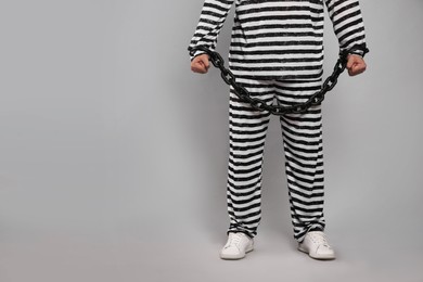 Prisoner in special uniform with chained hands on grey background, closeup. Space for text