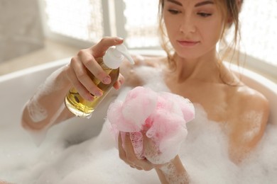 Beautiful woman pouring shower gel onto mesh pouf in bath indoors, focus on hands