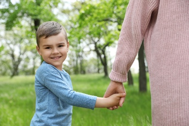Happy little child holding hands with his mother in park. Family time