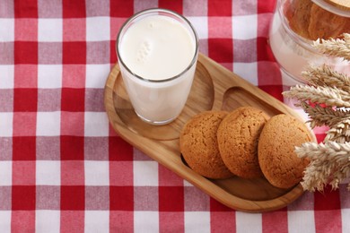 Glass of milk with cookies on red checkered tablecloth, above view. Space for text