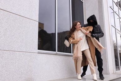 Woman fighting with thief while he trying to steal her bag near building, space for text. Self defense concept