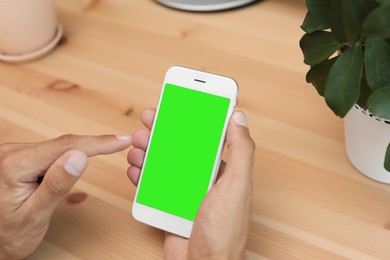 Image of Chroma key compositing. Man using smartphone with green screen at wooden table indoors, closeup. Mockup for design