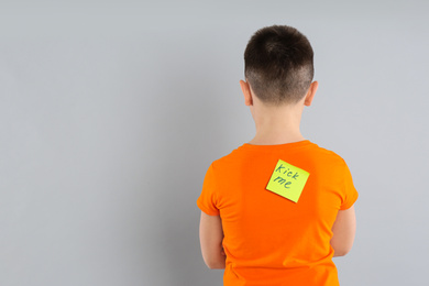 Photo of Preteen boy with KICK ME sticker on back against light grey background. April fool's day