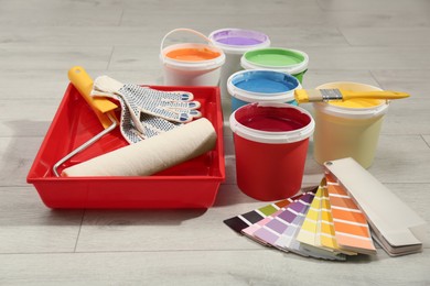 Buckets of paints, palette and decorator's tools on light wooden background