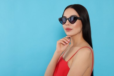 Attractive serious woman in fashionable sunglasses against light blue background. Space for text