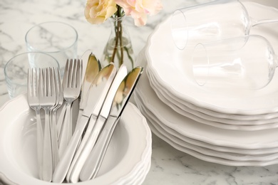Stacked plates, cutlery and glasses on white marble table, closeup
