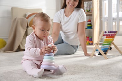 Cute baby girl playing with toy pyramid and mother on floor at home
