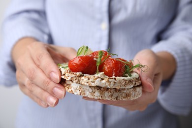 Photo of Woman holding crunchy buckwheat cakes with cream cheese, tomatoes and microgreens, closeup