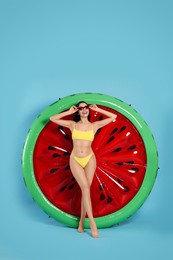 Young woman in stylish swimsuit near inflatable mattress against light blue background