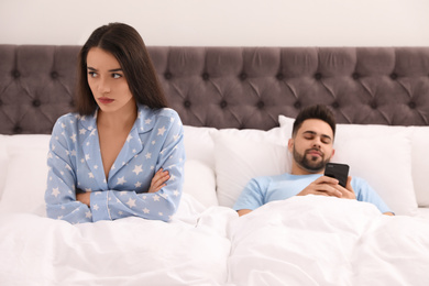 Young man preferring smartphone over his girlfriend in bed at home