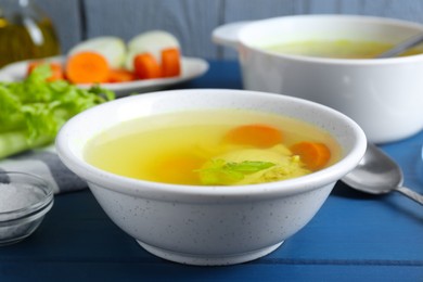 Photo of Delicious chicken bouillon with carrot and celery on blue wooden table, closeup