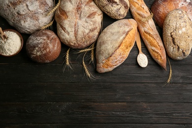 Different kinds of fresh bread on black wooden table, flat lay. Space for text