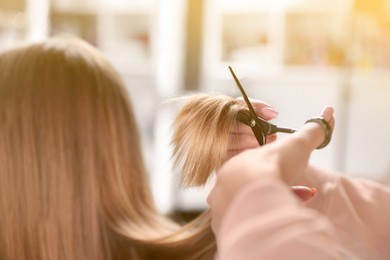 Hairdresser making stylish haircut with professional scissors in salon, closeup
