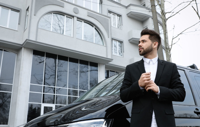 Handsome young man near modern car outdoors, low angle view
