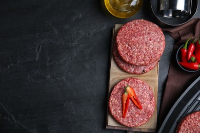 Raw hamburger patties with chili pepper on black table, flat lay. Space for text
