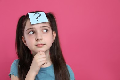 Photo of Pensive girl with question mark sticker on forehead against pink background. Space for text