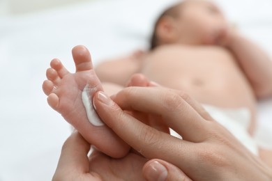 Mother applying body cream onto feet of her little baby, closeup