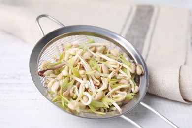 Photo of Mung bean sprouts in strainer and kitchen towel on white wooden table, closeup