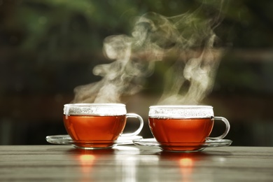 Cups of hot tea on wooden table against blurred background, space for text