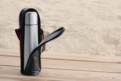 Photo of Metallic thermos in black stylish case on wooden surface outdoors, space for text