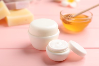 Jars of cream with natural beeswax component on pink wooden table, closeup