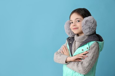 Cute little girl wearing stylish earmuffs on light blue background. Space for text