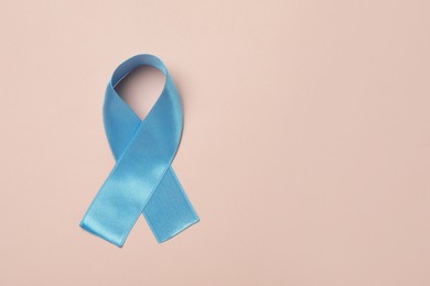 Photo of Light blue awareness ribbon on pale pink background, top view. Space for text