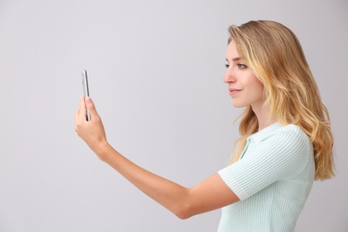 Young woman unlocking smartphone with facial scanner on grey background. Biometric verification