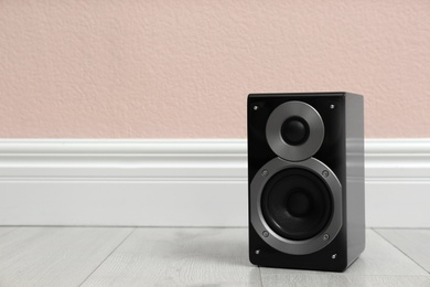 Modern powerful audio speaker on floor near pink wall. Space for text