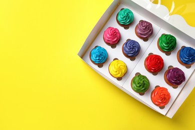 Box with different cupcakes on yellow background, top view. Space for text
