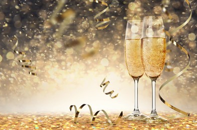 Image of Glasses with sparkling wine and shiny serpentine streamers against blurred festive lights , space for text 