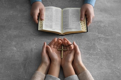 Boy praying and reading Bible with his godparents at grey table, closeup