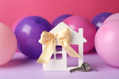 House model with bow, key and colorful balloons on violet table. Housewarming party