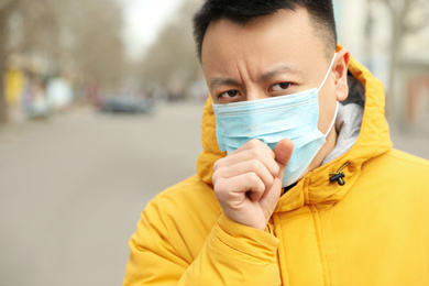 Asian man wearing medical mask on city street, space for text. Virus outbreak