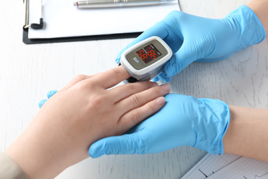 Photo of Doctor examining patient with fingertip pulse oximeter at white wooden table, closeup