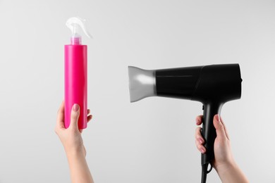 Photo of Woman holding spray bottle with thermal protection and hairdryer on white background, closeup