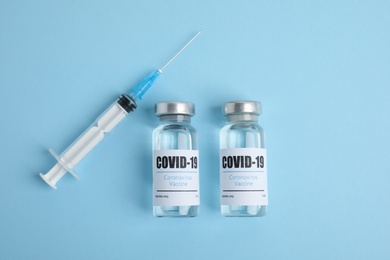 Vials with coronavirus vaccine and syringe on light blue background, flat lay
