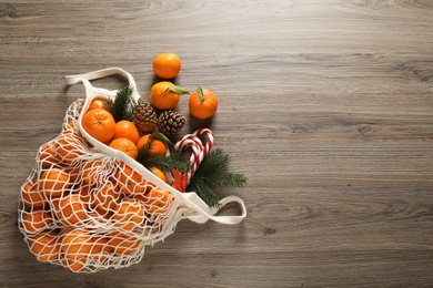 Photo of Flat lay Christmas composition with fresh tangerines in mesh bag on wooden table. Space for text