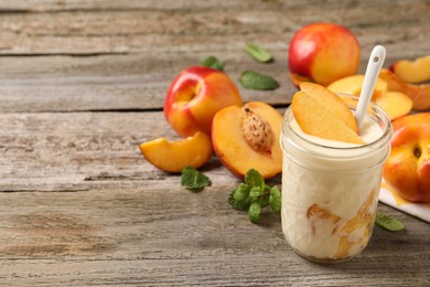 Tasty peach yogurt with pieces of fruit and spoon in glass jar on wooden table, space for text