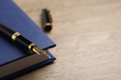 Beautiful fountain pen and blue notebook on wooden table, closeup. Space for text