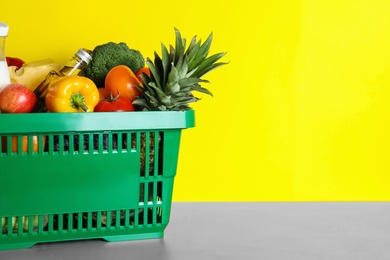 Shopping basket with grocery products on grey table against yellow background. Space for text