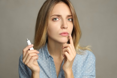Woman with herpes applying cream onto lip against  light grey background