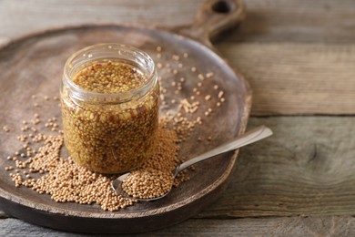 Photo of Jar and spoon of whole grain mustard on wooden table. Space for text