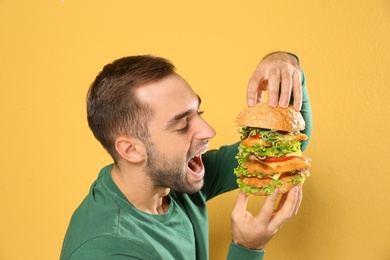 Young hungry man eating huge burger on color background