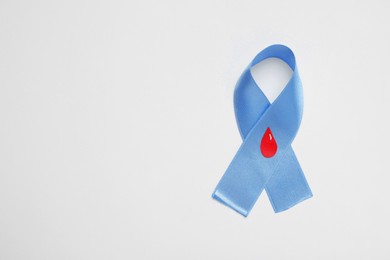 Photo of Light blue ribbon with paper blood drop on color background, top view and space for text. Diabetes awareness