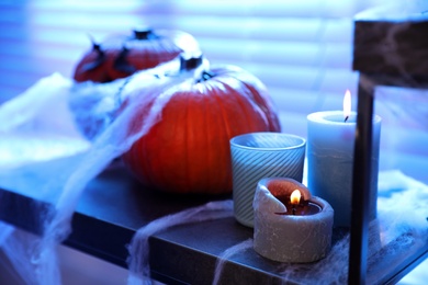 Candles, pumpkins and fake spiderweb on stand indoors. Halloween decoration