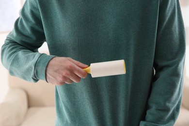 Photo of Man cleaning green sweatshirt with lint roller on light background, closeup