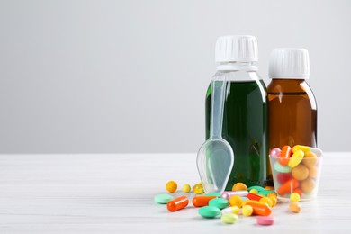Photo of Bottles of syrups with pills on wooden table against white background, space for text. Cough and cold medicine