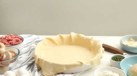 Photo of Raw dough and ingredients for meat pie on white table, space for text.